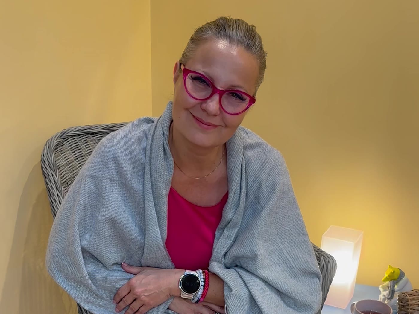 Aranyi Rita coach a fotelben ül, kendővel a vállán és mosolyogva figyel